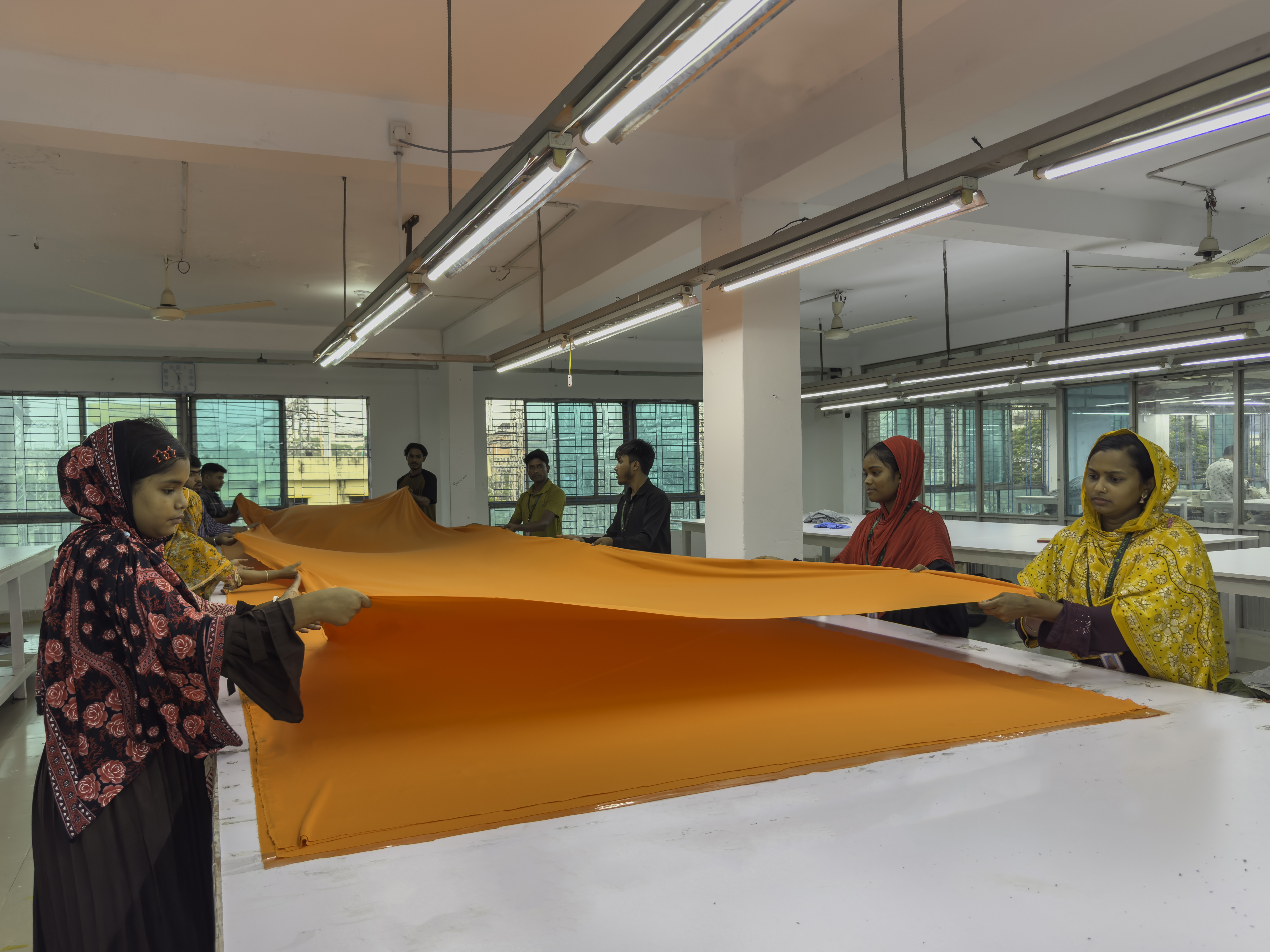 Workers laying out orange fabric on the cutting table